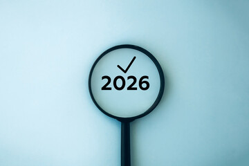 2026 under magnifying glass with check mark. Minimal composition symbolizing focus, planning, new year goals, and business strategy for the upcoming year.