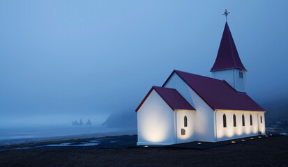 Quaint church in the coastal town of Vik, Iceland, on a foggy night with sea stacks in the distance
