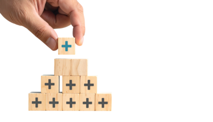 Hand placing a positive sign cube on a wooden pyramid, suggesting growth