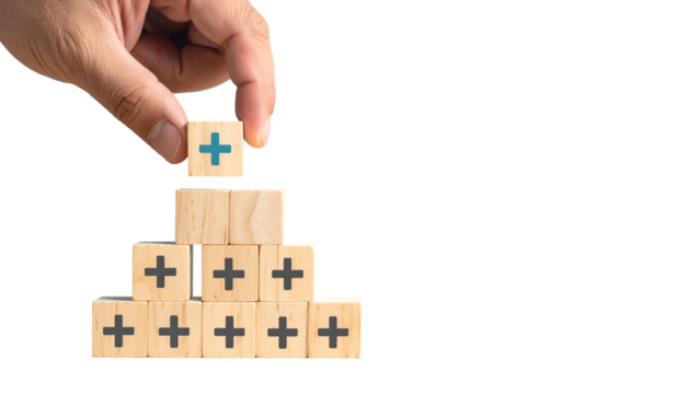 Hand placing a positive sign cube on a wooden pyramid, suggesting growth