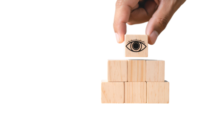 A hand places an eye symbol on top of wooden blocks forming a pyramid
