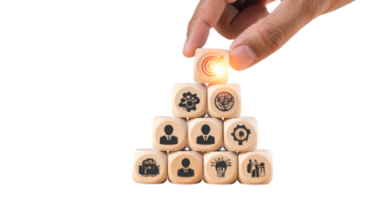 A hand places the top cube on a pyramid of wooden blocks with business-related symbols