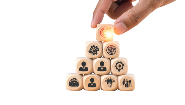A hand places the top cube on a pyramid of wooden blocks with business-related symbols