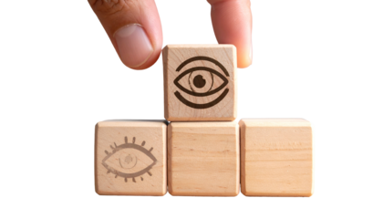 Hand placing an eye-symbol block atop a pyramid of wooden blocks on a black backdrop