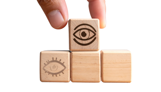Hand placing an eye-symbol block atop a pyramid of wooden blocks on a black backdrop