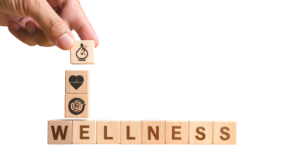 Hand arranging wooden blocks with health symbols atop "WELLNESS". Black background