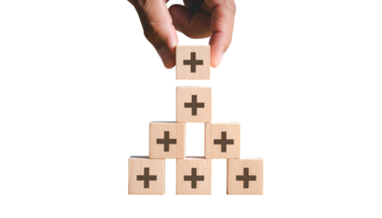 Hand arranging wooden blocks with plus signs into a pyramid on black background