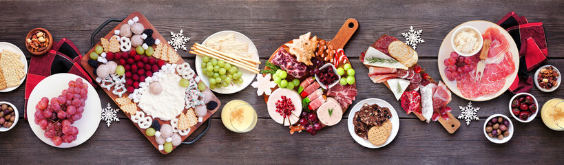Fototapeta na wymiar Christmas holiday charcuterie table scene on a dark wood banner background. Top down view. Variety of cheese, fruit and meat appetizers.