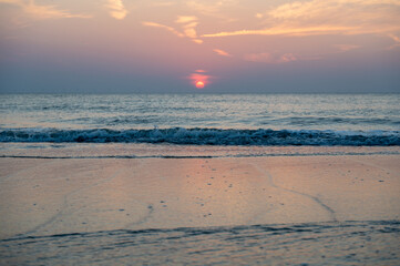 Sunset over the sea, with waves and sandy beach