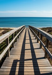 Obraz premium Scenic view of a weathered wooden boardwalk stretching along the coast, leading towards the vast, blue ocean under a bright, sunny sky ,seaside ,beach ,coastal