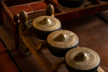 Detailed view of bronze gamelan gongs arranged on a wooden frame in warm indoor lighting