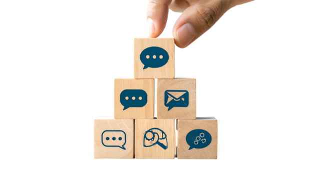 A hand places a speech bubble cube atop a wooden pyramid of communication icons