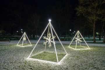 Minimalist Illuminated Christmas Pyramids with Snowflakes in Park on Dark Winter Night