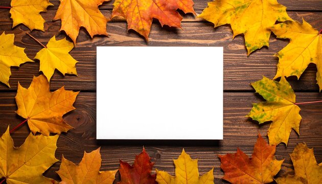 Autumn leaves frame a blank card on wooden background.