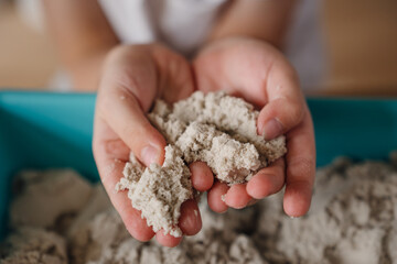close-up of a child's hands playing on a table with kinetic sand