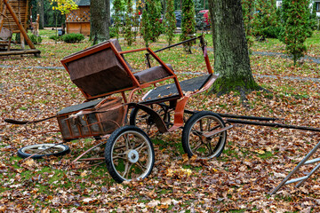 A rusted old-fashioned carriage with a wooden seat and wheels sitting on a grassy area with fallen...