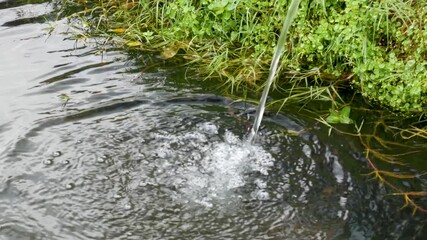 A clean 4K handheld shot of water splashing from a pipe into a small mountain pond used for irrigation. Ideal for agriculture, conservation, and detailed visual reference footage