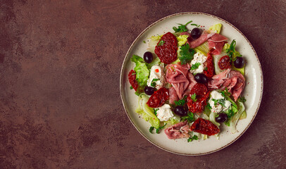 salad with dried tomatoes, prosciutto, soft cheese, olives, homemade, top view,