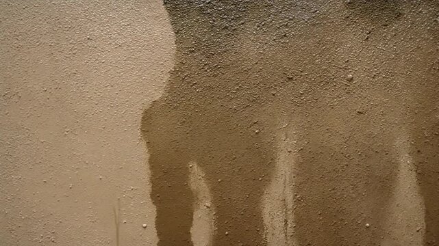 Abstract grunge background of a damp, textured earthen wall with water trickling down, creating streaks and patterns
