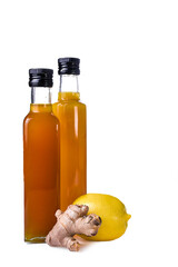 Natural homemade ginger lemon drink in glass bottles on white background. Fresh lemon and ginger root nearby. Healthy immunity booster beverage rich in vitamin C.