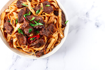 Udon noodles with Mongolian beef, green onions and vegetables, in a white plate, on a light background, homemade, no people,