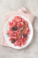 Freshly cut dried meat, served with olives and herbs, on a white plate, light background, no people,