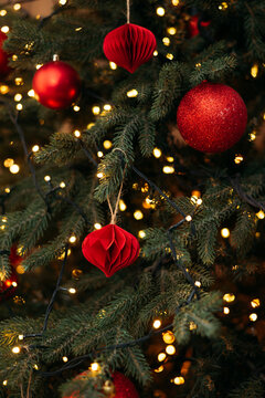 A close-up of a festive Christmas tree decorated with red ornaments, glowing fairy lights, and natural green pine needles.