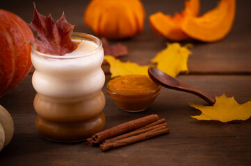 Cozy Autumn Pumpkin Spice Latte with Cinnamon Sticks, Pumpkin Butter, and Colorful Fall Leaves on Wooden Table