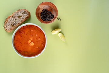 A bowl of vegan soup with tofu sits on a green table with a wooden bowl and a slice of bread. The soup is red. Concept of comfort and warmth, as the soup