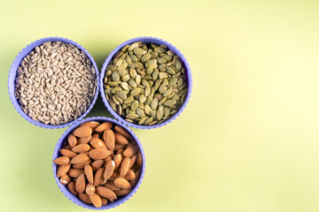 Three purple bowls of different nuts and seeds on a green background. The bowls are arranged in a triangular pattern