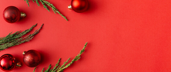 Banner made of Red Christmas balls decoration and tree branches on red background. New Year greeting card. Minimal style. Flat lay, top view, copy space.