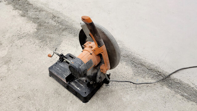 A portable, heavy-duty chop saw or abrasive cut-off machine designed for precision cutting of metal profiles, featuring an orange motor housing and a large abrasive disc guard - Powered by Adobe