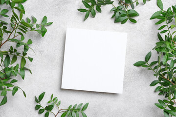 Square blank card mockup on a textured concrete surface, surrounded by lush green leaves. Perfect for invitations, branding, and flyer presentations