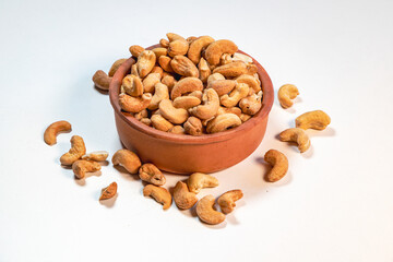 Roasted cashew nuts in clay bowl on white background