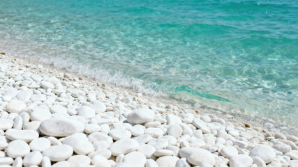 Soft white pebbles line a tranquil shore, where gentle waves softly lap against the beach under a clear blue sky. This serene scene captures a peaceful moment by the ocean