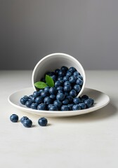 Vibrant blue berries overflowing from a simple white dish, topped with a crisp green accent leaf. Healthy summer snack on a clean surface ,vegan, delicious, dessert