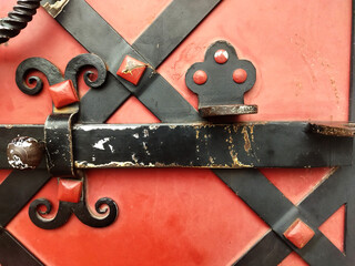 Old forged black iron latch with rivets on red wooden door, vintage metalwork detail, rustic architecture close-up