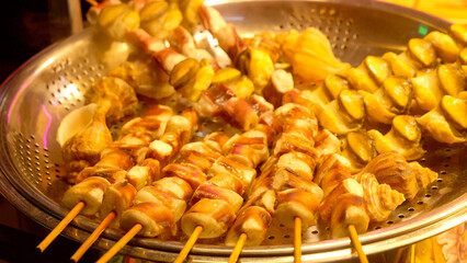 Seafood skewers and whelks are steaming on a tray at a street food stall in Seoul