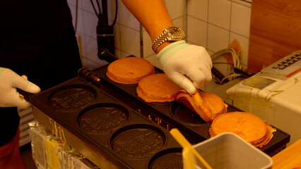 Vendor hands removing Korean street food pancakes from a hot cooking pan