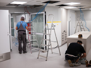 An electrician runs cables over a suspended ceiling in a new room