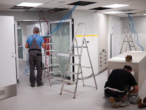 An electrician runs cables over a suspended ceiling in a new room