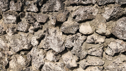 A rough, dry-stacked stone wall, built from local, porous, pinkish-grey volcanic tuff, showcasing a distinct spongy and rustic texture