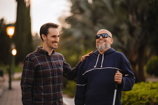 Blind Man and His Young Helper Laughing Together in the Park. Concept of Disability and Friendship
