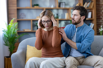Woman clutching temples in severe headache while partner sits close on sofa offering comfort and...
