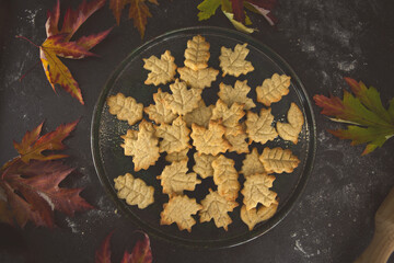 Homemade baked cookies in leaf shapes on a dark plate with autumn leaves. Cozy fall dessert, homemade recipe, seasonal baking, and sweet handmade gift idea.