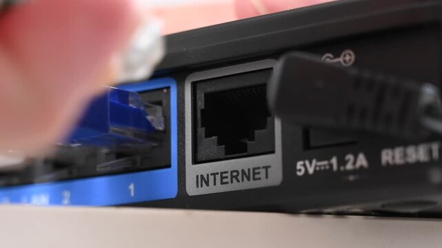 A woman pulls a cable out of an internet port on a router. 