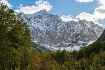 The Slovenian mountains covered in the first snow of the season, with colorful autumn trees in the foreground creating a perfect seasonal contrast