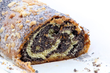 Close-up of a cross-section of a traditional sweet roll (strudel, poppy seed roll) with a generous dark poppy seed filling. The pastry is covered with white sugar icing and sprinkled.