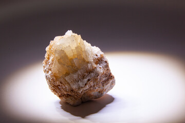 Close-up of an uncut piece of rock or crystal with yellowish-beige crystalline facets. The stone is brightly lit from below or from the side, creating a dramatic effect against a dark.