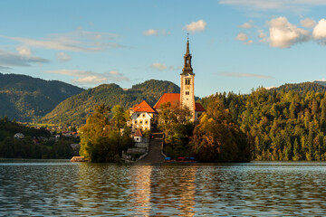 Fototapeta premium Peaceful sunset view of Lake Bled with the island church and castle reflecting in calm waters, surrounded by soft autumn light and mountain silhouettes